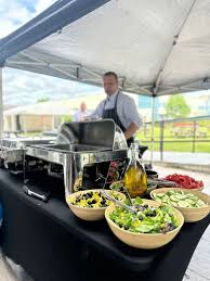 Outdoor buffet catering station with fresh salads and covered serving dishes